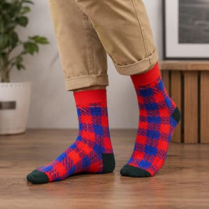 Könnte beinhalten: Ein Paar wadenhohe Socken mit einem leuchtend roten und blauen Karomuster. Die Socken haben ein einfarbig rotes Bündchen am oberen Rand sowie eine dunkelgrüne, verstärkte Zehen- und Fersenpartie, die einen Kontrast zum Karomuster bildet.