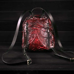 May include: A red leather backpack with black straps and buckles. The backpack has a textured, wrinkled design.