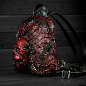May include: A red leather backpack with a skull design. The backpack has black straps and buckles.