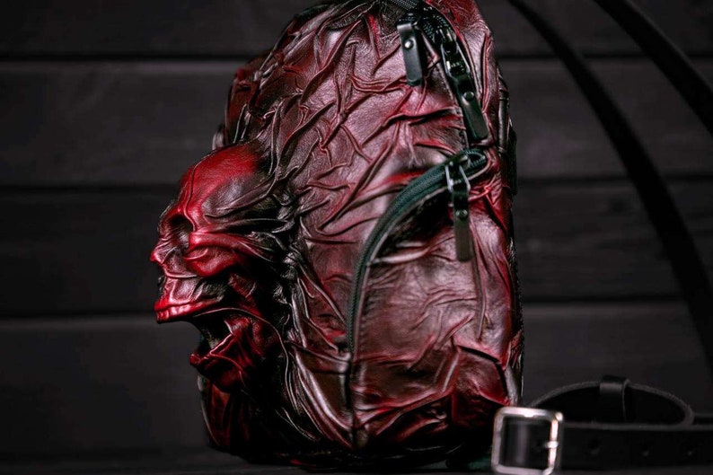 May include: A red leather backpack with a skull design. The backpack has a zipper closure and adjustable straps.