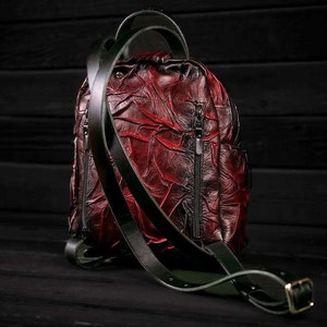 May include: A red leather backpack with black straps and zippers. The backpack has a textured, wrinkled design.