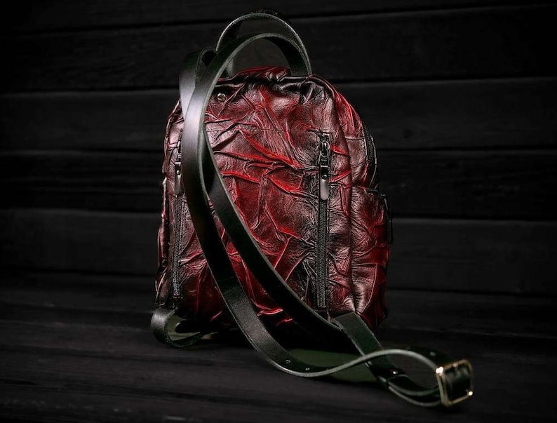 May include: A red leather backpack with black straps and zippers. The backpack has a textured, wrinkled design.