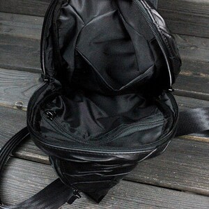 May include: A black quilted crossbody bag with a zippered pocket on the front and a long adjustable strap. The bag is open and the inside is visible.