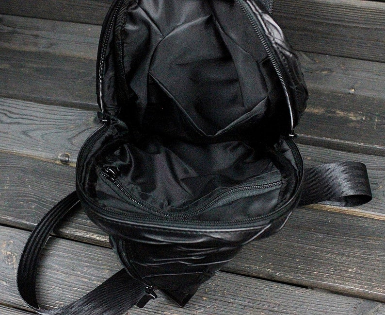 May include: A black quilted crossbody bag with a zippered pocket on the front and a long adjustable strap. The bag is open and the inside is visible.