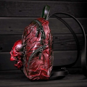 May include: A red leather backpack with a skull design. The backpack has black straps and zippers.