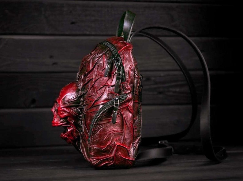 May include: A red leather backpack with a skull design. The backpack has black straps and zippers.