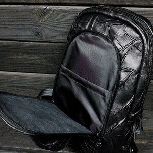 May include: A black leather backpack with a textured design. The backpack has a large main compartment and a smaller front pocket.