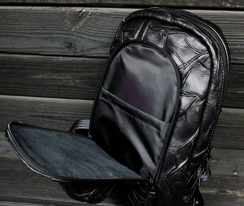 May include: A black leather backpack with a textured design. The backpack has a large main compartment and a smaller front pocket.
