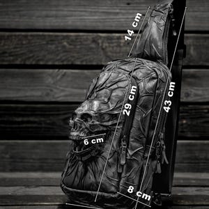 May include: Black leather crossbody bag with a skull design. The bag measures 17 inches wide, 29 inches tall, and 8 inches deep. The strap is 43 inches long and 14 inches wide.