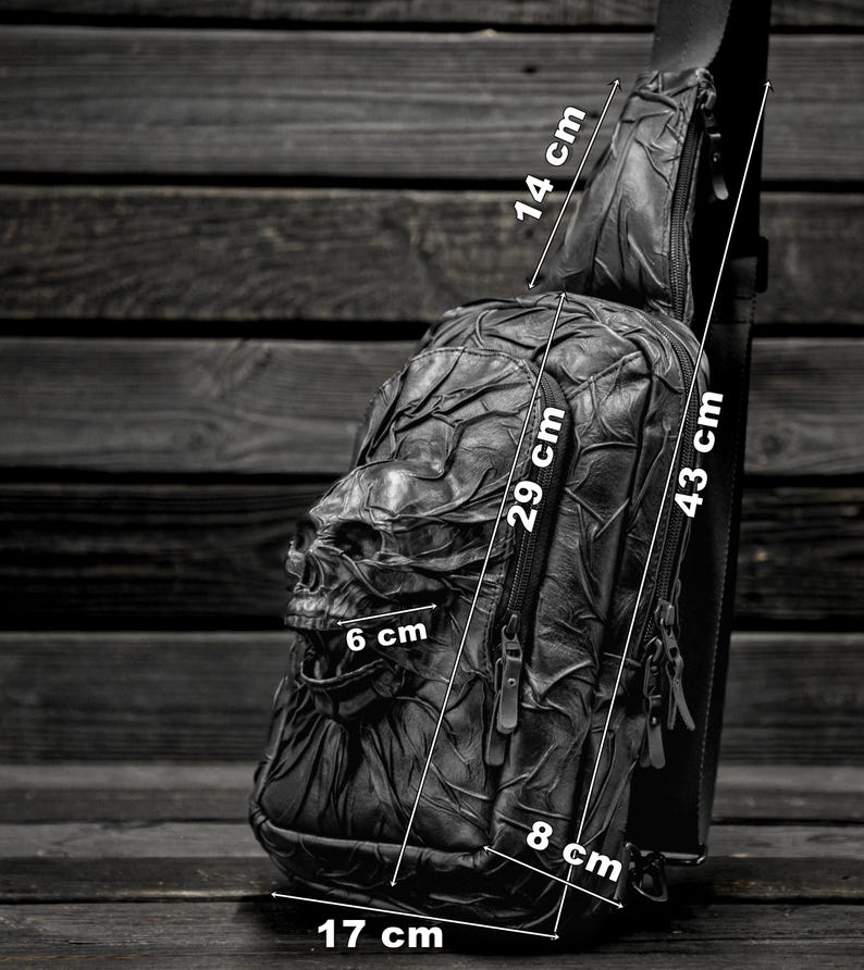 May include: Black leather crossbody bag with a skull design. The bag measures 17 inches wide, 29 inches tall, and 8 inches deep. The strap is 43 inches long and 14 inches wide.