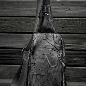 May include: A black leather crossbody bag with a textured design and adjustable strap.