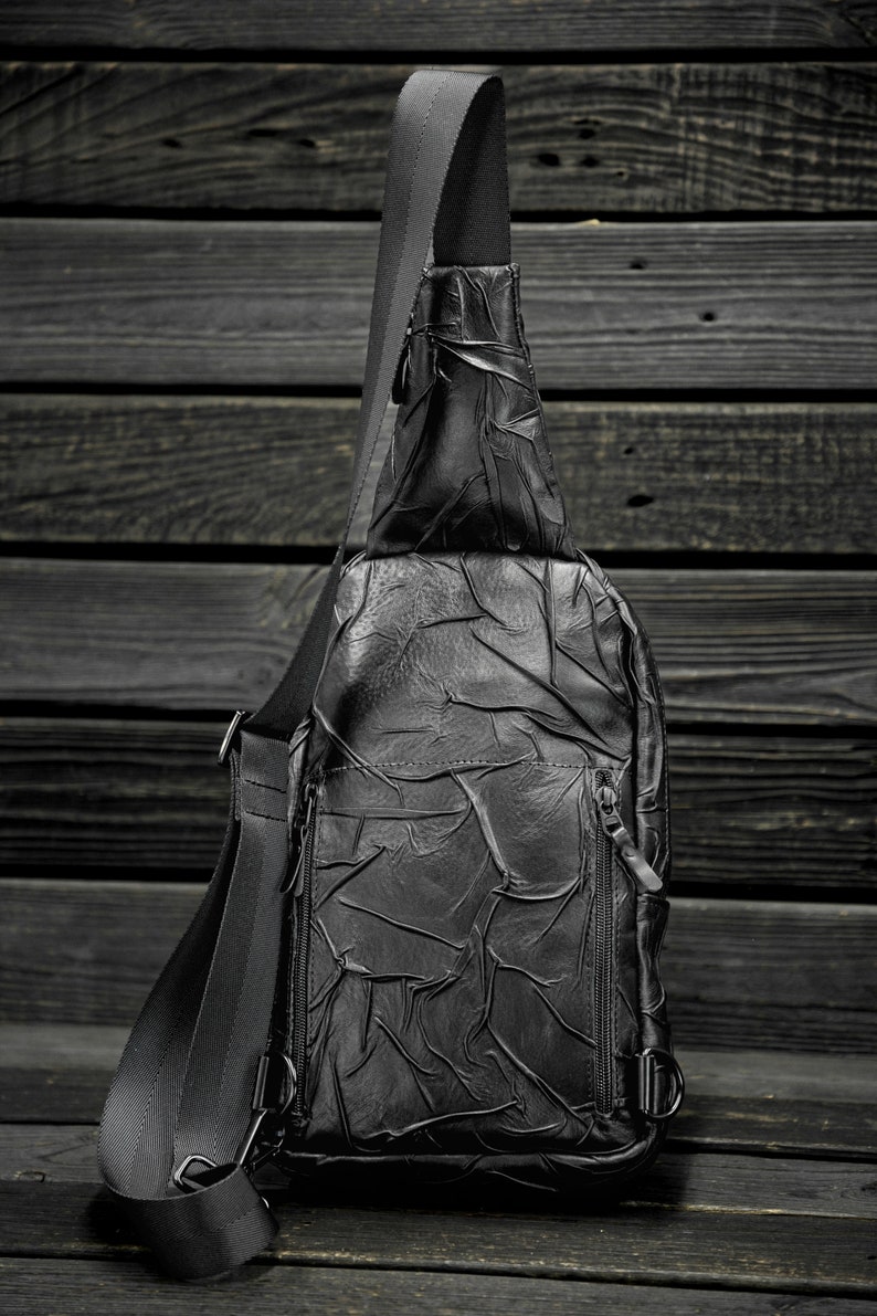 May include: A black leather crossbody bag with a textured design and adjustable strap.