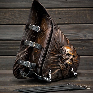 Puede incluir: Una alforja de moto de cuero marrón con un diseño de calavera. La bolsa tiene múltiples hebillas y correas.