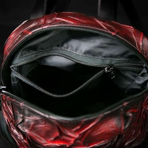 May include: Red leather backpack with a zippered pocket and a black lining. The backpack is open and the inside is visible.