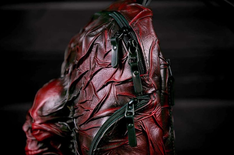 May include: A red leather backpack with a textured, scaly design. The backpack has black zippers and straps.