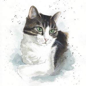 May include: Watercolor painting of a tabby cat with green eyes. The cat is lying down with its head turned to the side. The background is a light blue watercolor wash with white speckles. The cat's name, "Kuma", is written in cursive at the bottom of the painting.