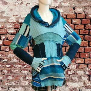 May include: A blue and black patchwork sweater with a cowl neck and long sleeves. The sweater is made from different types of knit fabric and has a distressed look.