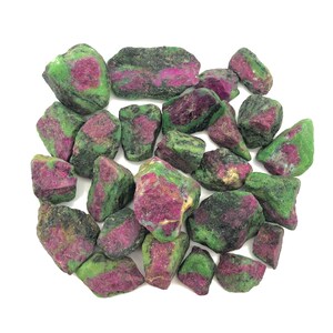 Könnte beinhalten: Eine Sammlung von rohen Zultanit-Edelsteinen in Grün und Pink. Die Steine sind in verschiedenen Größen und Formen und haben eine natürliche, unpolierte Oberfläche.