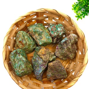 May include: A collection of seven green, brown, and red gemstone rocks in a woven basket. The rocks have a rough, natural texture.