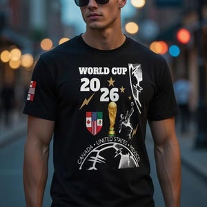 Puede incluir: Camiseta negra con el texto "WORLD CUP 2026" y gráficos que incluyen un trofeo, las banderas de Canadá, Estados Unidos y México. La camiseta también presenta un rayo y una silueta de jugador de fútbol.