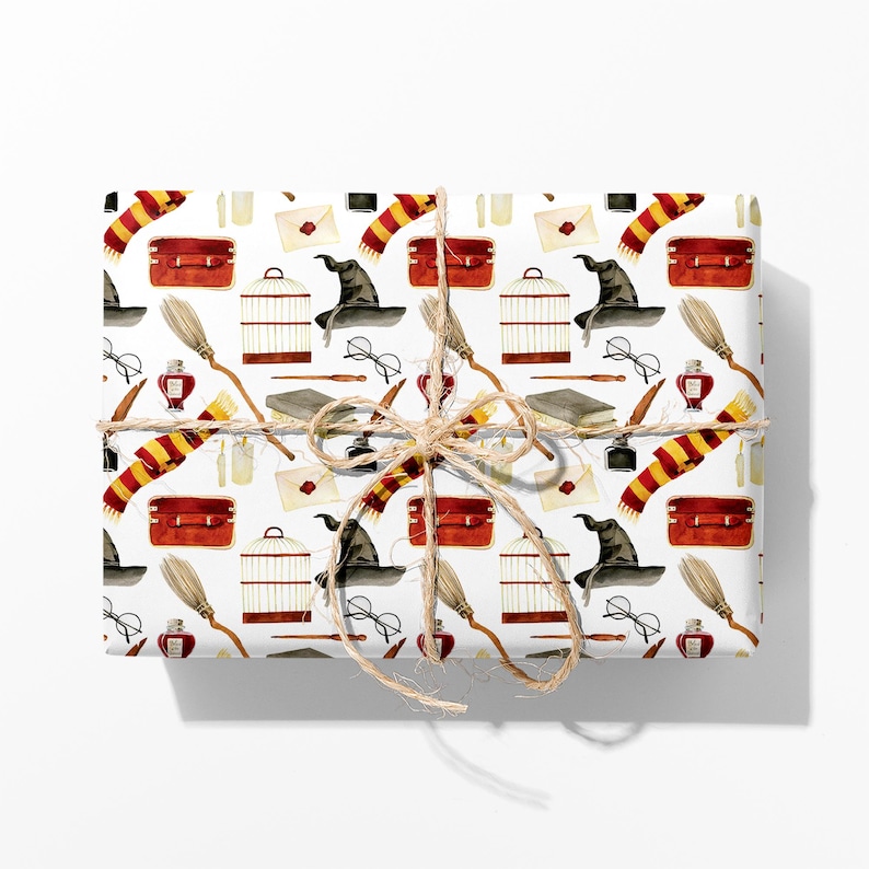 May include: Gift-wrapped package featuring a white background with a repeating pattern of watercolor illustrations. The pattern includes a red suitcase, a black witch hat, a broom, a scarf, glasses, and a birdcage. The package is tied with twine.