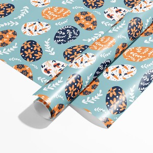 May include: A blue and white wrapping paper with a repeating pattern of orange, white, and blue eggs. The eggs have different designs, including flowers, carrots, and leaves.