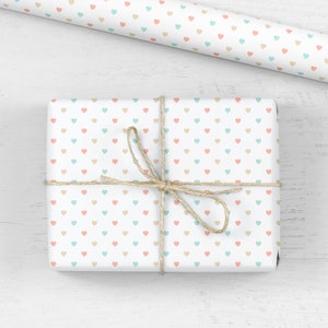 May include: A white gift box wrapped in paper with a pattern of small pastel pink, blue, and beige hearts. The box is tied with twine.
