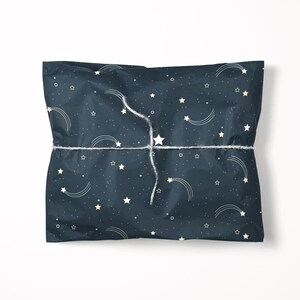 May include: A wrapped gift with a dark blue background covered in white and yellow stars and shooting star designs. The gift is tied with white twine.
