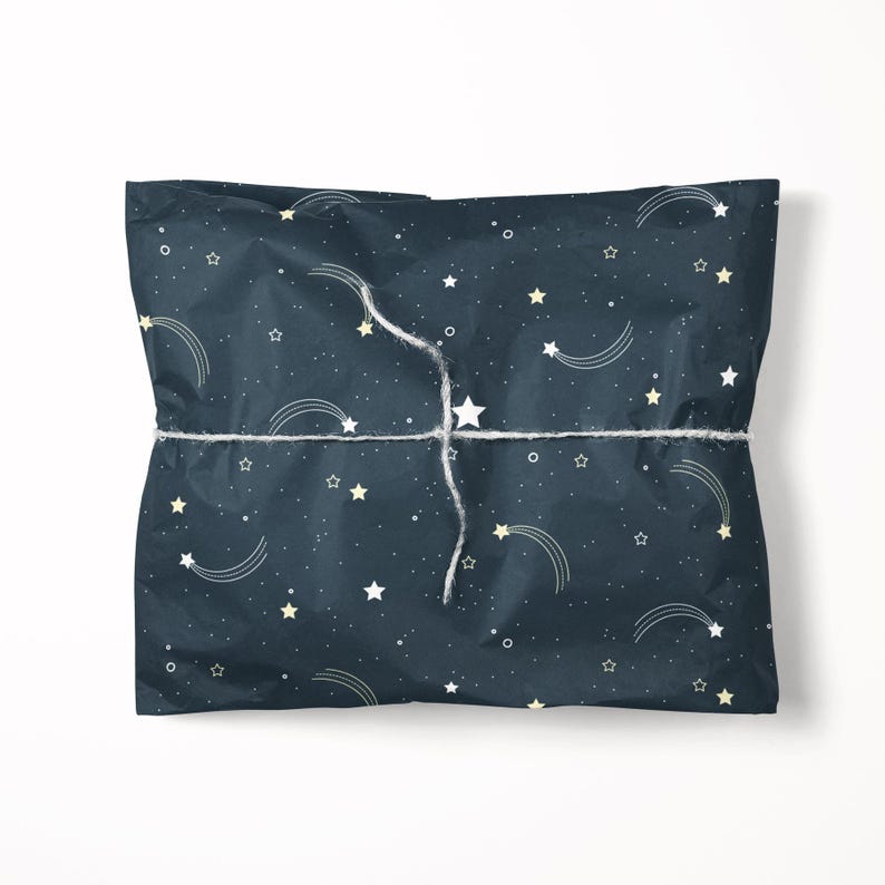 May include: A wrapped gift with a dark blue background covered in white and yellow stars and shooting star designs. The gift is tied with white twine.