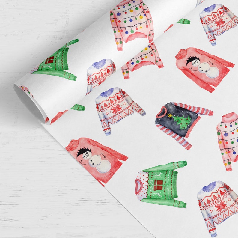 May include: A roll of white wrapping paper featuring a repeating watercolor pattern of various sweaters. Designs include red sweaters with snowmen, green sweaters with gift boxes, dark sweaters with Christmas trees, and sweaters with light bulbs.