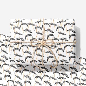 May include: A rectangular gift box wrapped in white paper featuring a repeating pattern of black mustaches on thin wooden sticks. The package is tied with a natural tan jute twine string arranged in a decorative bow centered on the top surface.