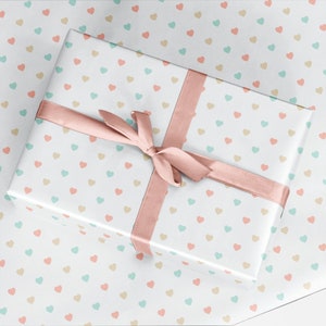 May include: A white gift box with a pink ribbon and a pattern of small pastel hearts. The box is wrapped in white paper with a repeating pattern of small hearts in shades of pink, blue, and beige.