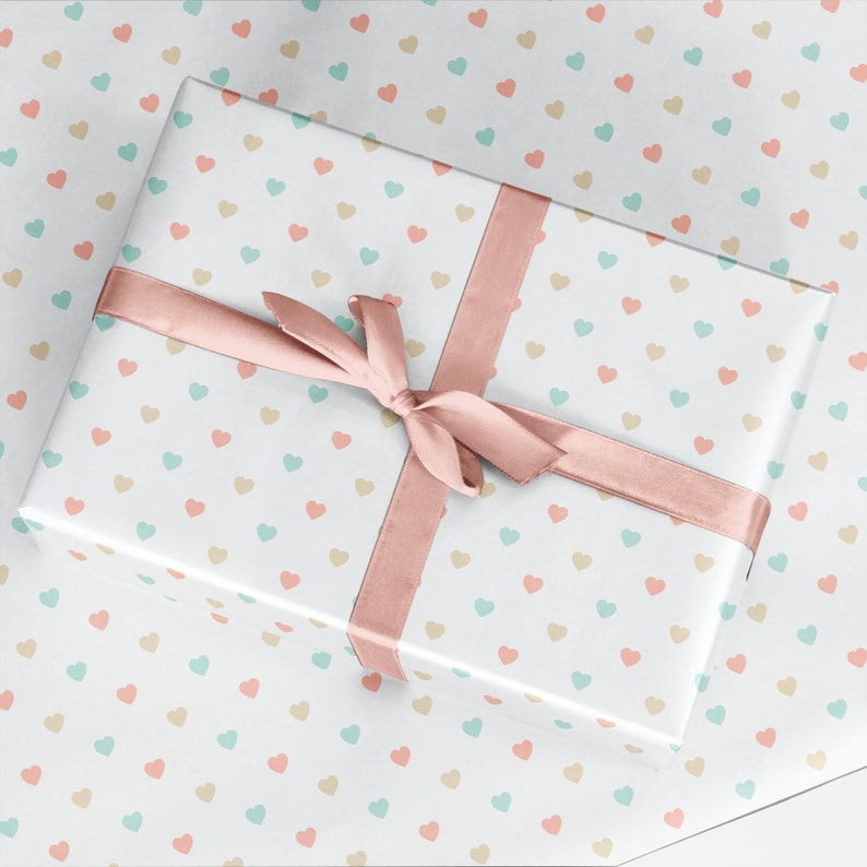 May include: A white gift box with a pink ribbon and a pattern of small pastel hearts. The box is wrapped in white paper with a repeating pattern of small hearts in shades of pink, blue, and beige.