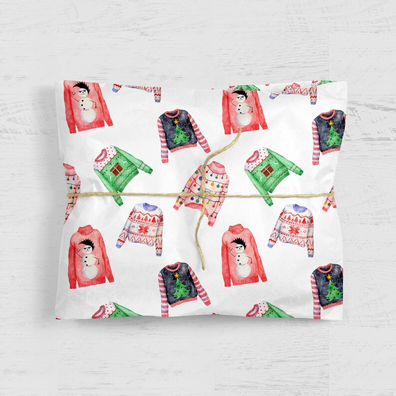May include: White wrapping paper featuring a repeating watercolor pattern of various holiday sweaters, including red snowman designs, green sweaters with gift boxes, dark blue tree patterns, and pink sweaters with colorful string light graphics.