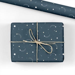 May include: A wrapped gift with a navy blue background, adorned with white stars and shooting star designs. The gift is tied with natural twine. A roll of matching wrapping paper is visible in the background.