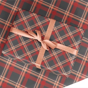 K&ouml;nnte beinhalten: Eine Geschenkbox, verpackt in rot-schwarzem kariertem Geschenkpapier mit einem pfirsichfarbenen Band, das zu einer Schleife gebunden ist.