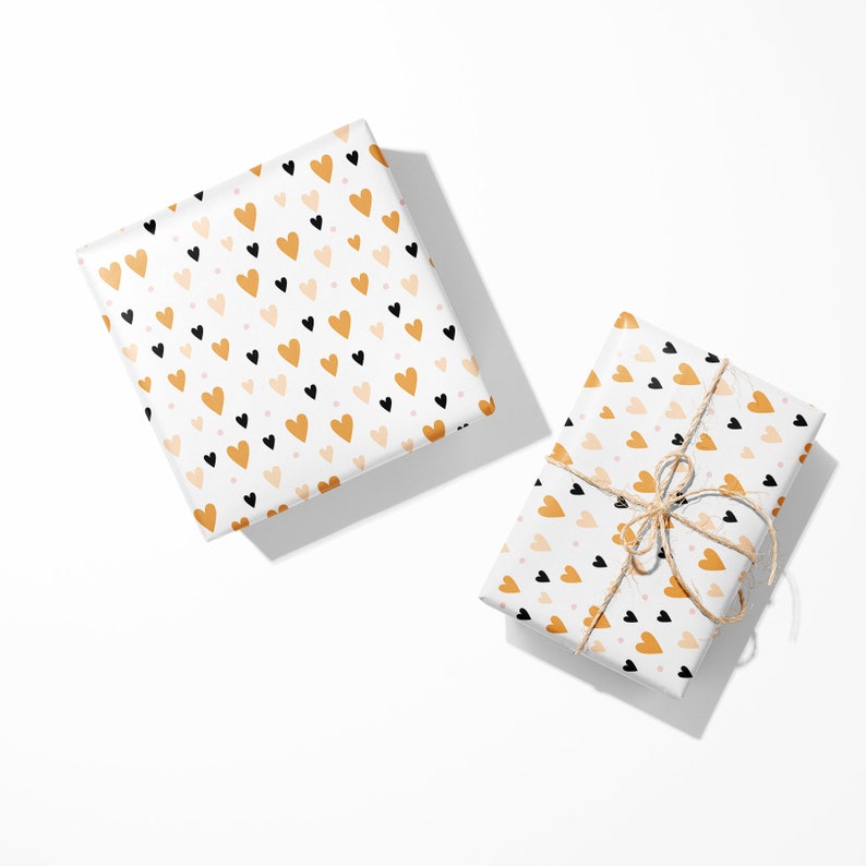 May include: Two gift boxes wrapped in white paper with a repeating pattern of black, gold, and pink hearts. One box is tied with twine. The gifts are on a white background.