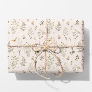 May include: A rectangular gift box wrapped in light cream paper featuring a repeating pattern of green ferns, wildflowers, and small butterflies. The package is tied with a natural tan jute twine string arranged in a bow at the centre.