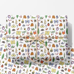 May include: A rectangular gift wrapped in white paper featuring a repeating colourful pattern of various insects, snails, and worms, tied with a natural brown jute twine string tied in a bow at the centre of the package.