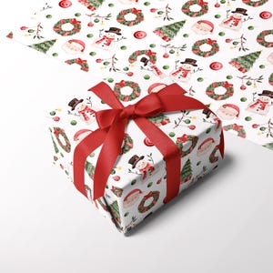 May include: A rectangular gift box wrapped in white paper featuring a repeating Christmas pattern of snowmen, wreaths, Santa faces, and pine trees, tied with a wide red satin ribbon. The same patterned paper is visible unfolded in the background.