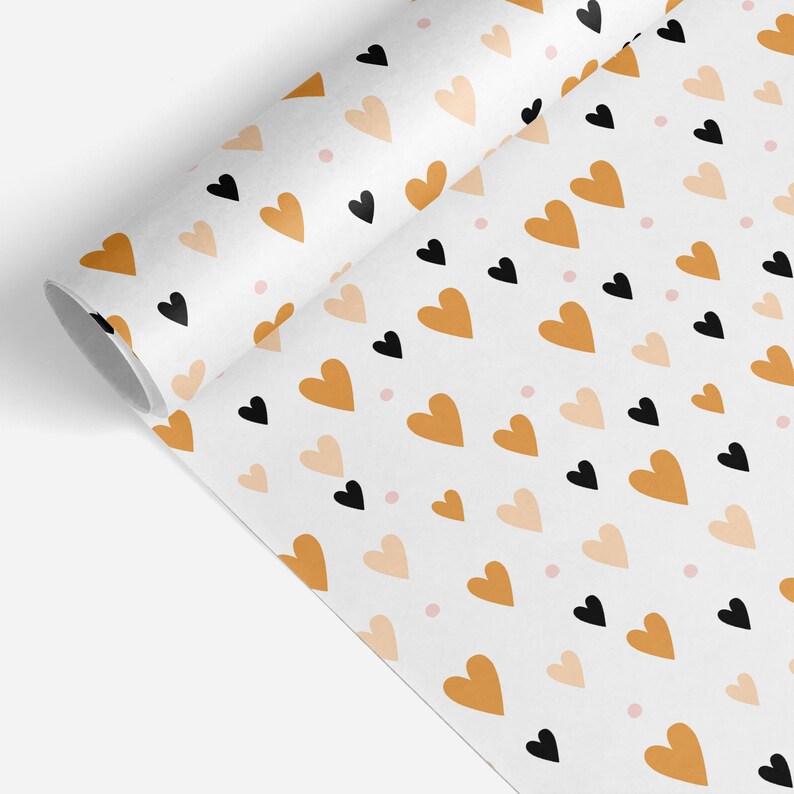 May include: A roll of white wrapping paper with a repeating pattern of hearts in black, tan, and peach colors, along with small pink dots. The paper is partially unrolled, revealing the pattern.