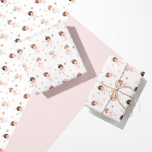 May include: Wrapping paper featuring a repeating watercolor pattern of ballerinas in pink tutus and small gold stars on a white background. One square package is wrapped in the paper, and a rectangular package is tied with thin brown twine.