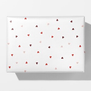 May include: White gift wrap with a scattered pattern of red, pink, and maroon hearts.