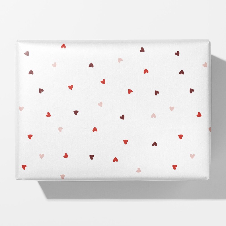 May include: White gift wrap with a scattered pattern of red, pink, and maroon hearts.