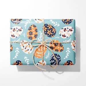 May include: A blue gift box with a pattern of orange and blue Easter eggs. The box is tied with twine.