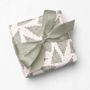 May include: A square gift box wrapped in light pink paper featuring a repeating pattern of green pine trees and small orange stars, tied with a wide, sage green satin ribbon bow centered on the top surface of the package.
