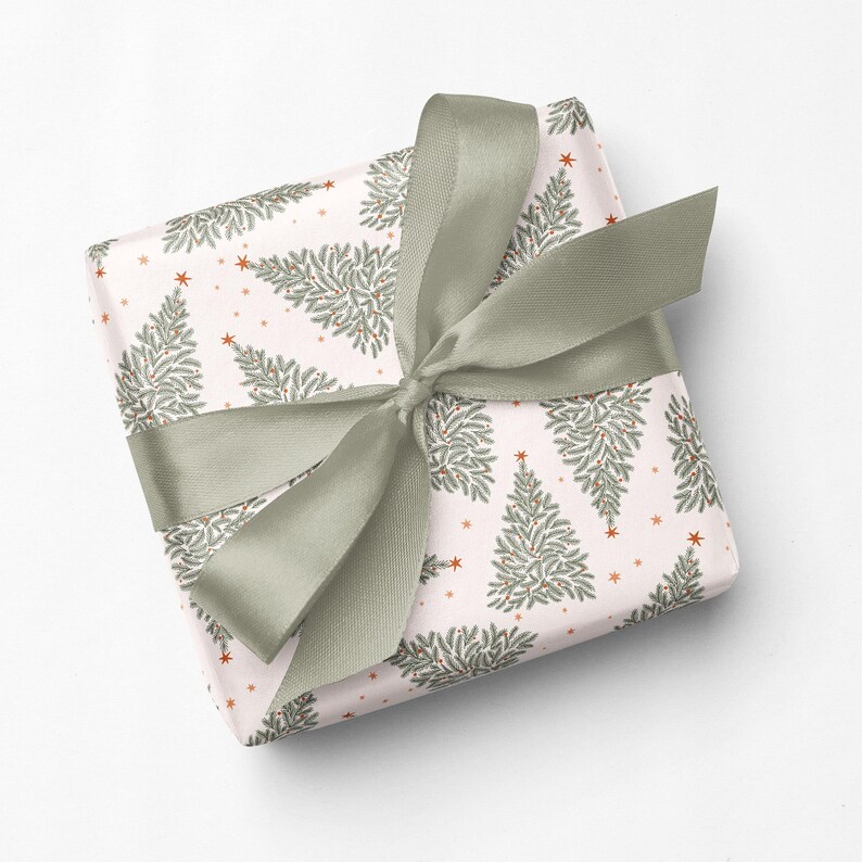 May include: A square gift box wrapped in light pink paper featuring a repeating pattern of green pine trees and small orange stars, tied with a wide, sage green satin ribbon bow centered on the top surface of the package.
