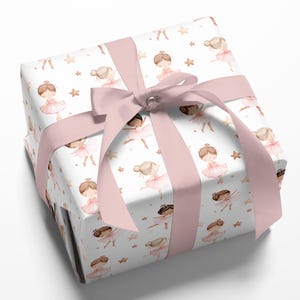 May include: A square gift box wrapped in white paper featuring a repeating pattern of watercolor illustrations of ballerinas in pink tutus and small gold stars, tied with a wide, smooth, light pink satin ribbon bow on the top surface.