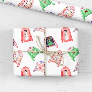 May include: A rectangular gift box wrapped in white paper featuring a repeating watercolor pattern of various holiday sweaters, including designs with snowmen, Christmas trees, and string lights, tied with a thin natural jute twine string.