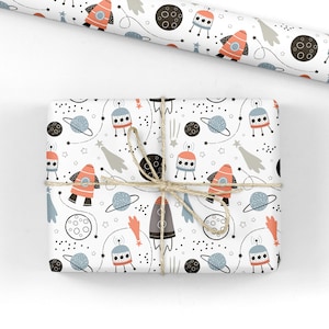 May include: White gift wrap with a repeating pattern of rockets, planets, stars and comets. The rockets are orange and grey, the planets are black and white, and the stars are white. The comets are grey and white.
